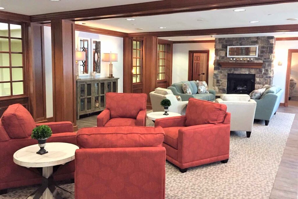 Common area in senior living community featuring red and tan club chairs, blue sofas, wide wood trim and a stone fireplace.